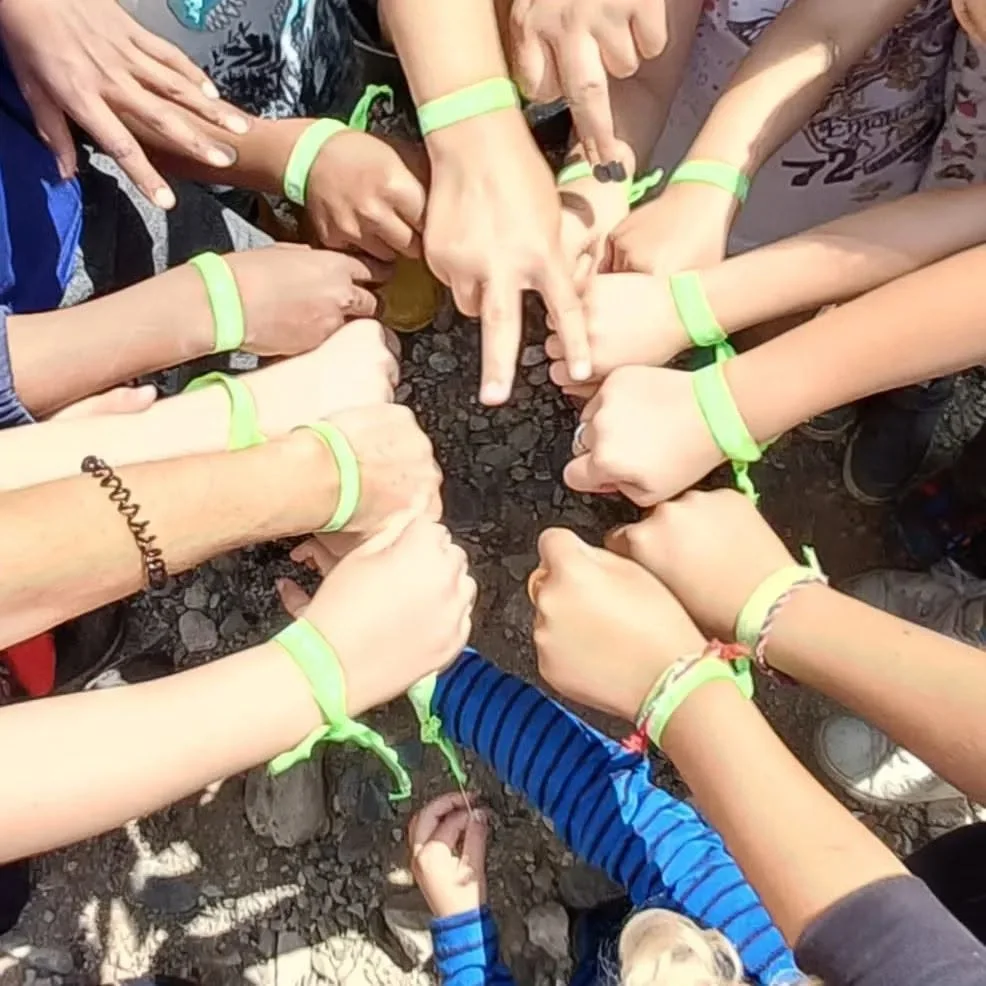 Un grup reuneix les mans amb polseres verdes durant una activitat a l’aire lliure.
