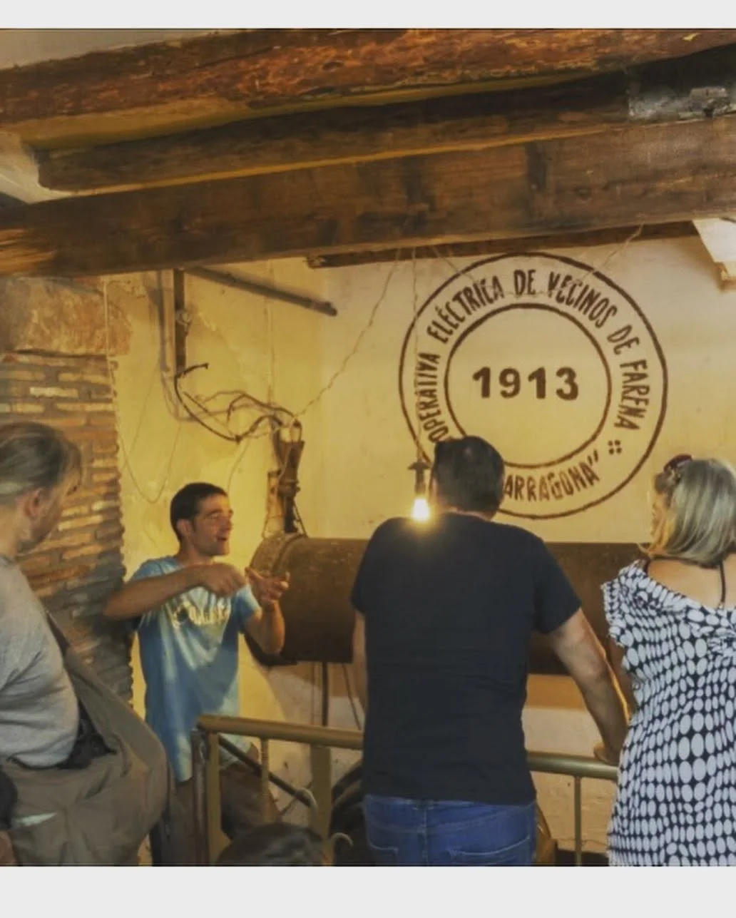 Un guia explica el patrimoni hidràulic a un grup al costat del rètol de la cooperativa elèctrica de Farena de 1913.